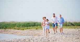 Uma família multigeração em férias a pé à beira do lago, correndo.