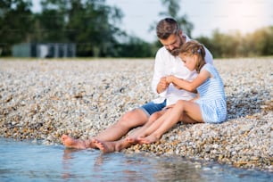 湖や海のほとりに座っている休日の父と小さな娘の側面図。