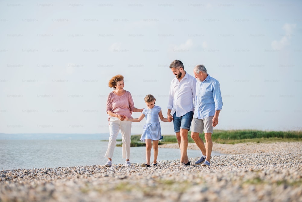 Una familia multigeneracional en unas vacaciones caminando por el lago, tomados de la mano.