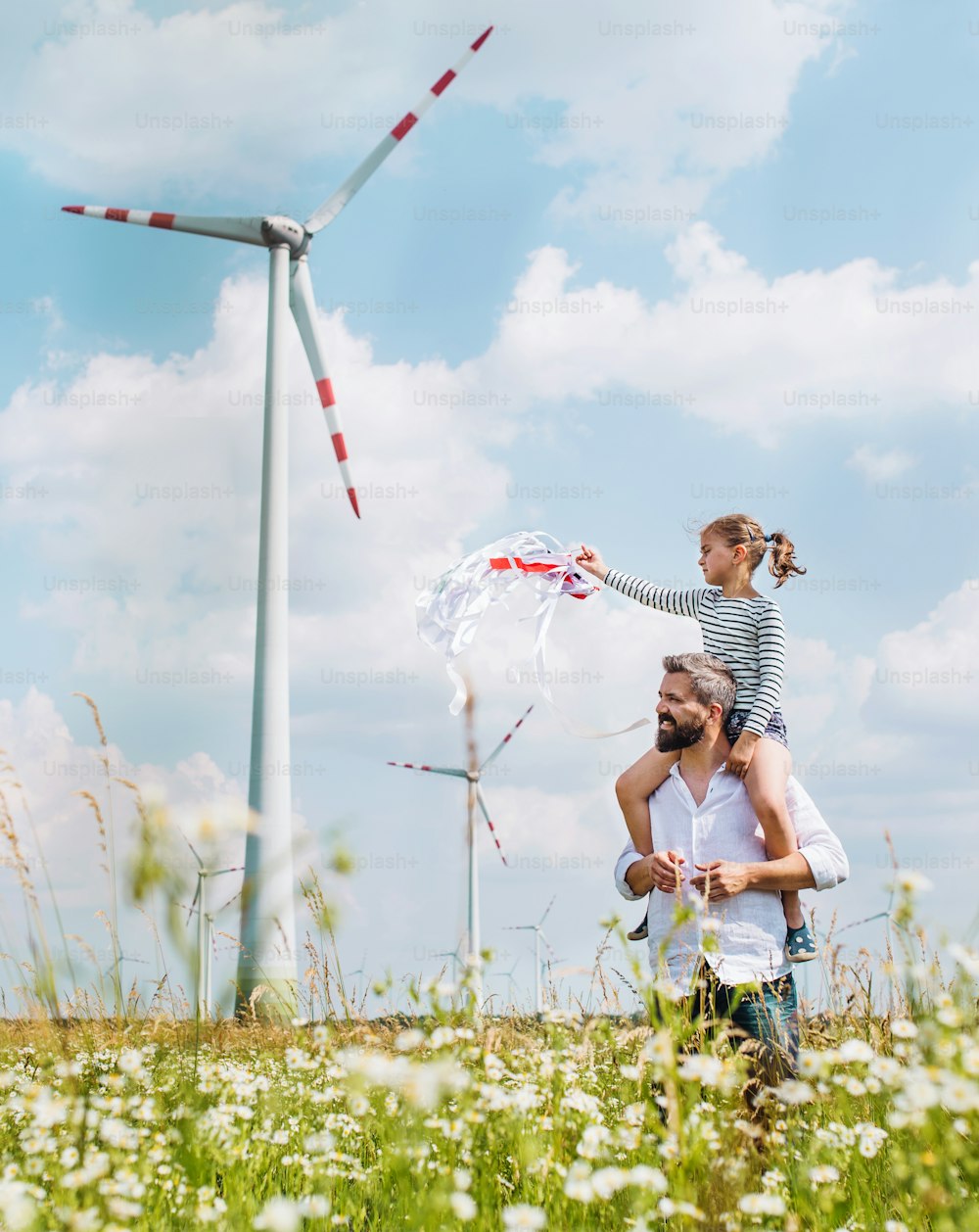 Père mûr avec une petite fille marchant sur le champ d’un parc éolien, lui donnant un tour de ferroutage.
