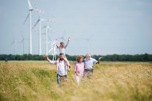 A front view of multigeneration family walking on field on wind farm.