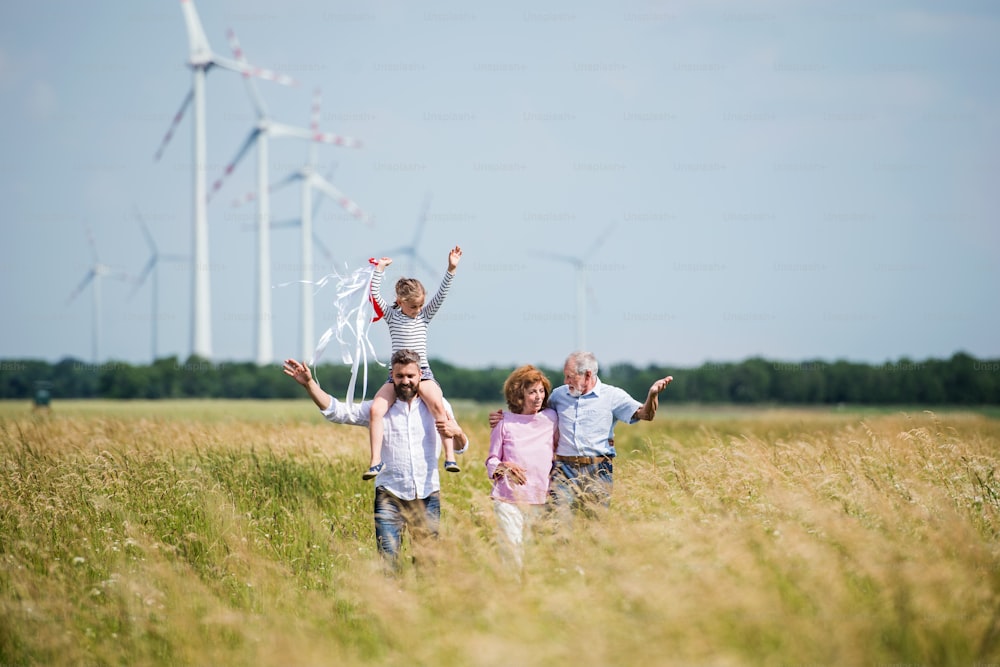 Une vue de face d’une famille multigénérationnelle marchant sur un champ sur un parc éolien.
