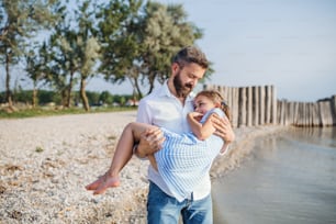 Un padre maduro que lleva a una hija pequeña en unas vacaciones junto al lago, caminando.