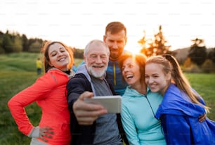 Un groupe de personnes en forme et actives se reposant après avoir fait de l’exercice dans la nature, en prenant un selfie avec un smartphone.