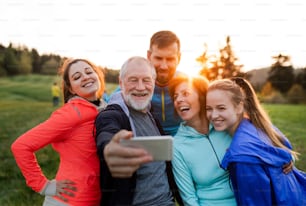 A group of fit and active people resting after doing exercise in nature, taking selfie with smartphone.