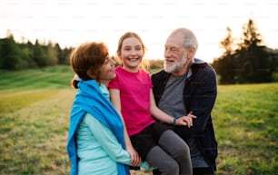An active senior couple with cheerful granddaughter standing in nature at sunset.