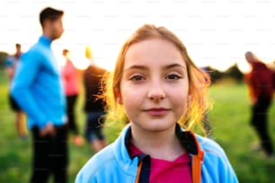 A portrait of small girl with large group of people doing exercise in nature, resting.