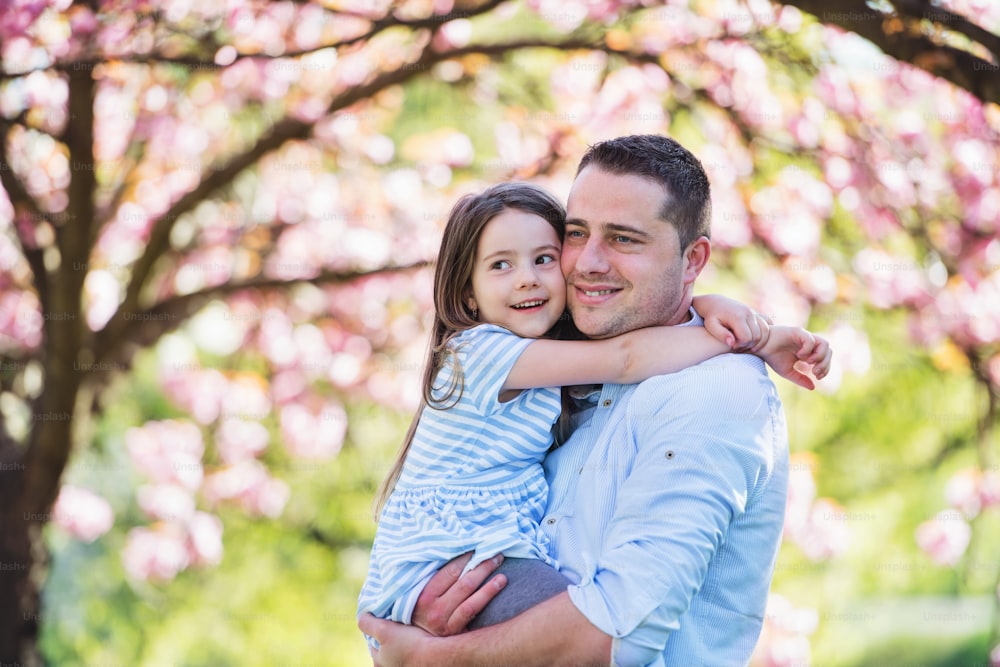 A young father holding small daughter outside in spring nature.