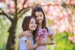 Two small girls standing outside in spring nature, hugging. Copy space.