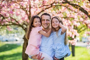 Young father holding small daughters outside in spring nature, looking at camera.