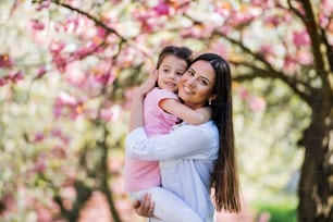 A young mother holding small daughter outside in spring nature.