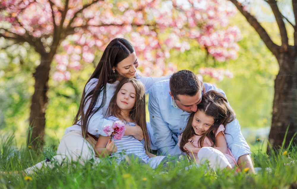 Front view of young parents with small daugthers sitting outside in spring nature.
