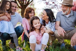 Front view of three generation family sitting outside in spring nature, talking.