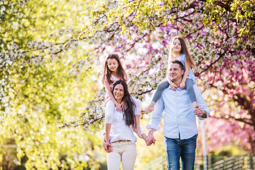 Família de jovens pais com pequenos daugthers andando ao ar livre na natureza da primavera.