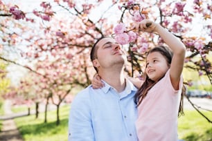 A young father holding small daughter outside in spring nature.