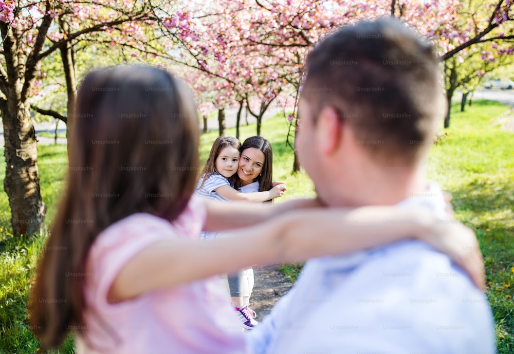 Famiglia di giovani genitori con piccoli daugthers in piedi fuori nella natura primaverile, divertendosi.