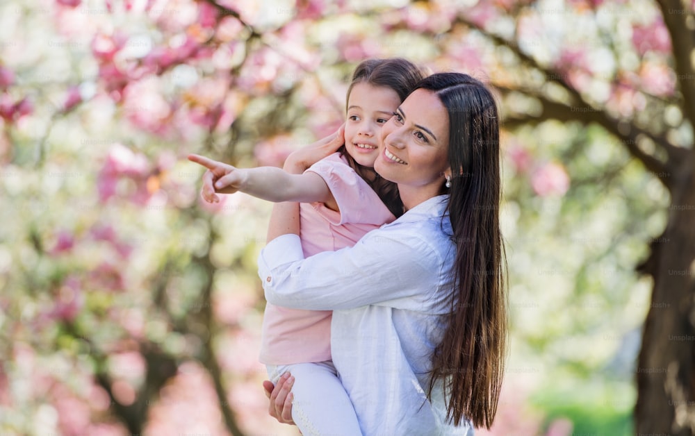 A young mother holding small daughter outside in spring nature.