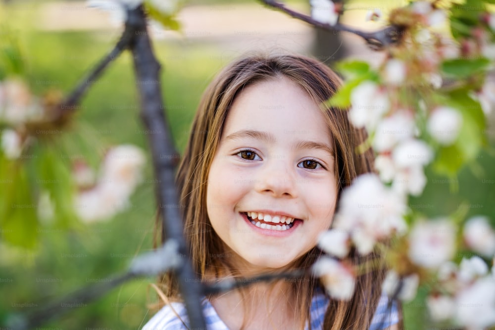春の自然の中で外に立ってカメラを見ている陽気な小さな女の子の正面図。