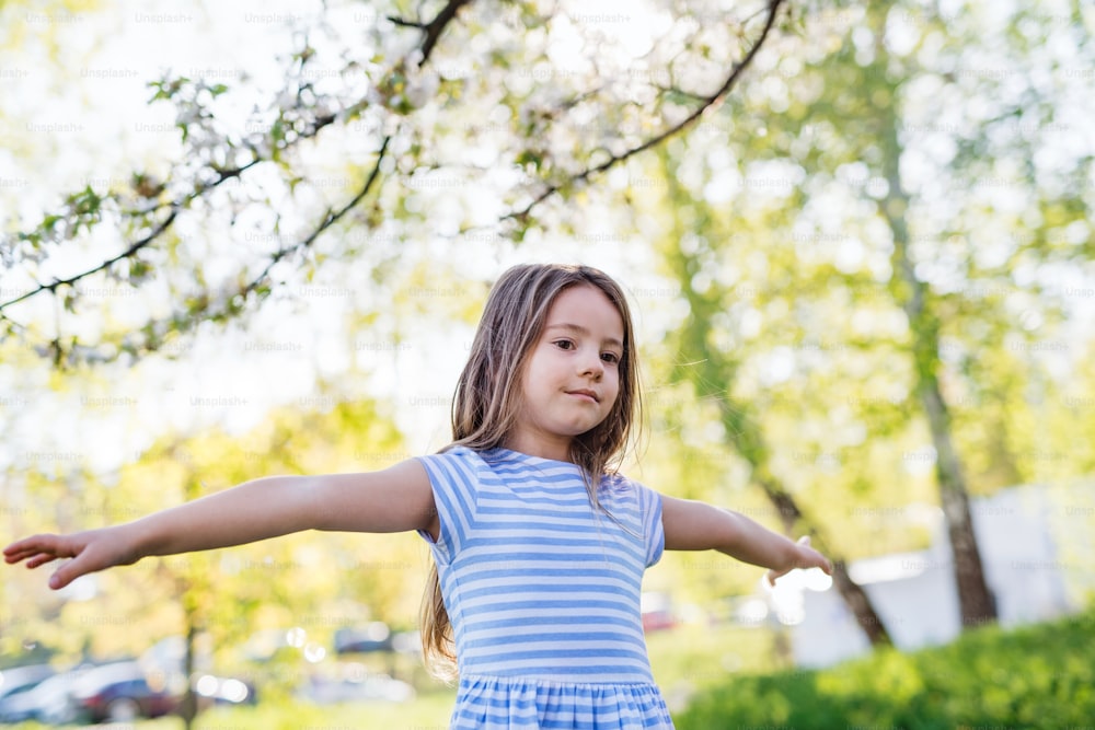 A front view of cheerful small girl playing outside in spring nature.