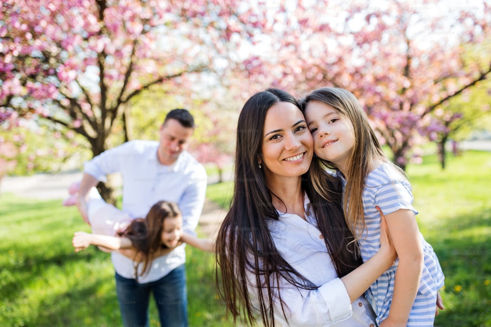 Familie von jungen Eltern mit kleinen Töchtern, die draußen in der Frühlingsnatur stehen und Spaß haben.