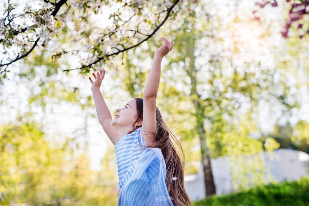 Una vista lateral de una niña pequeña alegre corriendo afuera en la naturaleza primaveral.