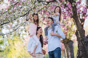Familie von jungen Eltern mit kleinen Töchtern stehen draußen in der Frühlingsnatur.