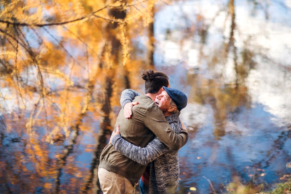A senior father and his son standing in nature, hugging.