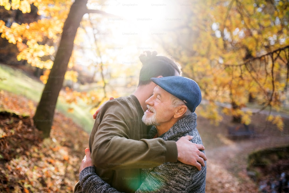 A senior father and his son on walk in nature, hugging at sunset.