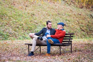 Senior father and his young son sitting on bench in nature, talking.