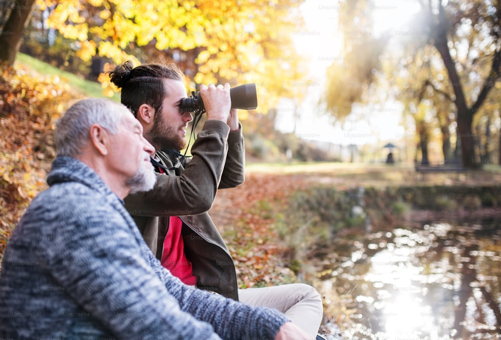 Senior father and his son with binoculars sitting on bench in nature, talking.