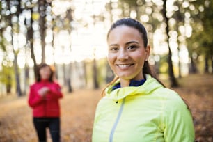 A portrait of young female runner standing outdoors in forest in autumn nature.