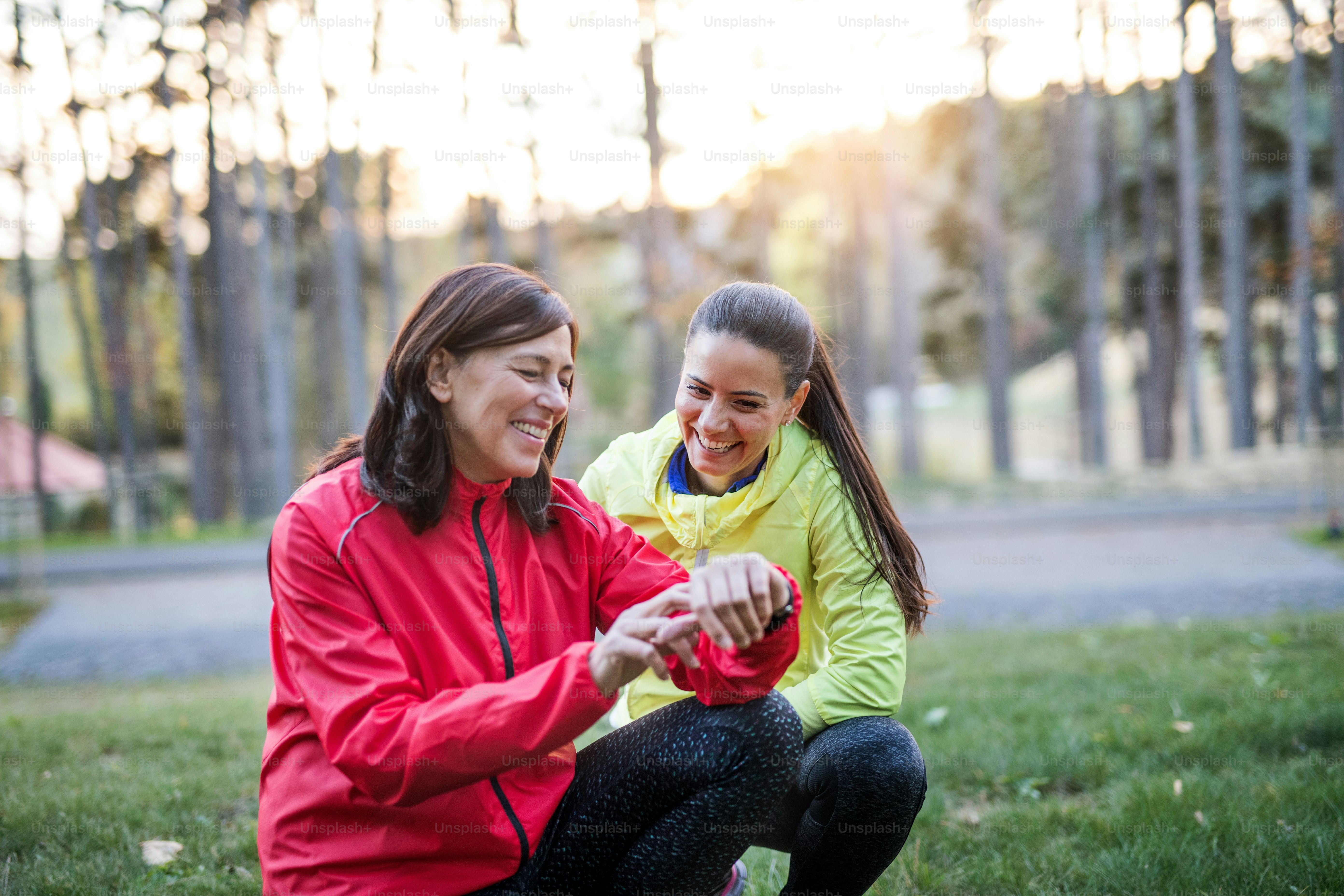 Two female runners with smartwatch outdoors in park in autumn nature at sunset, measuring or checking the time.