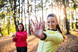 Two active female runners stretching outdoors in forest in autumn nature after he run.