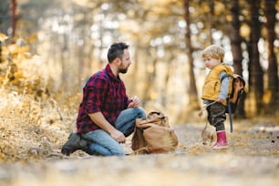 Un padre maduro con mochila y un hijo pequeño en un bosque otoñal, hablando.