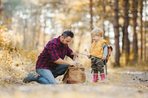 Ein reifer Vater mit einem kleinen Sohn in einem Herbstwald, der etwas aus einem Hinterhof nimmt.
