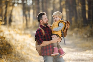 A mature father standing and holding a toddler son in an autumn forest, talking.