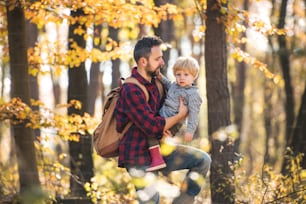 Um pai maduro com um filho pequeno em uma caminhada na floresta em um dia ensolarado de outono.