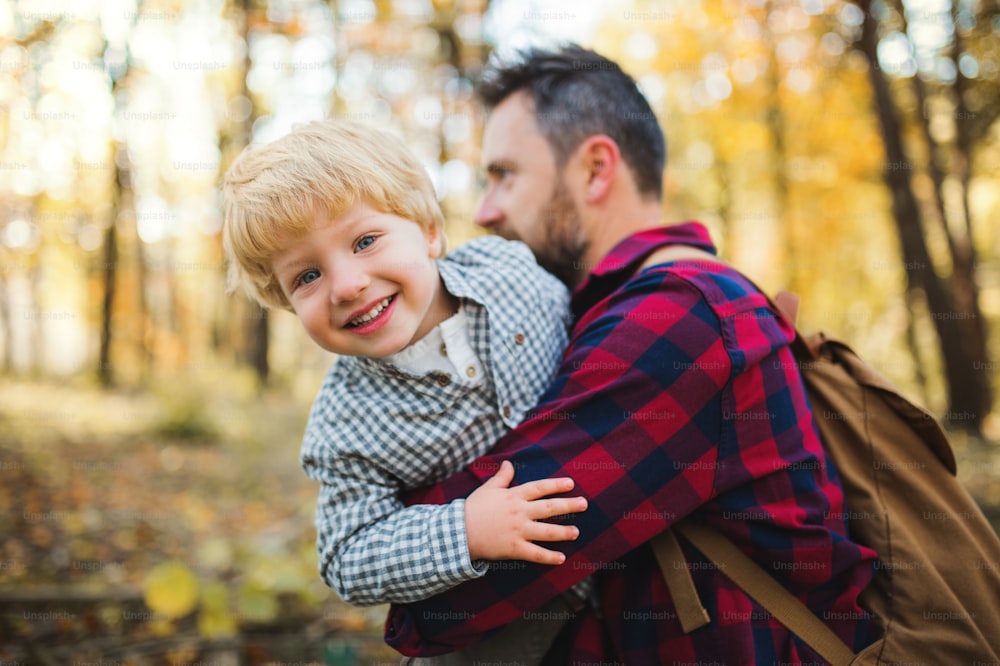 A mature father standing and holding a toddler son in an autumn forest, having fun.
