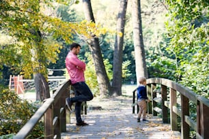 작은 아들을 둔 아버지가 가을 공원에서 산책을 하고 다리 위에 서 있다.