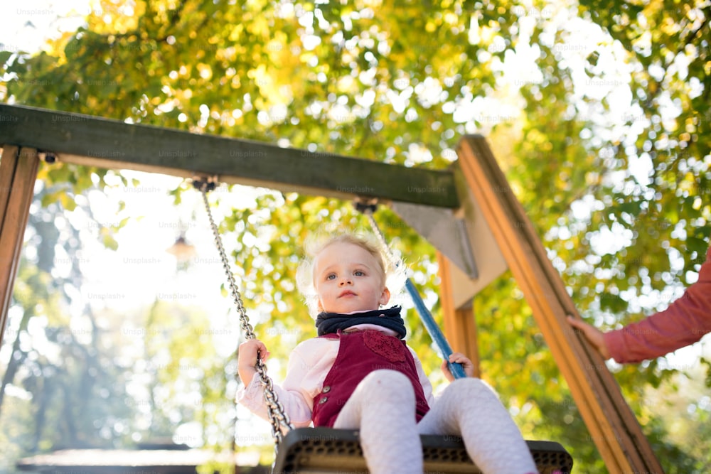 Una piccola bambina allegra con un padre irriconoscibile su un'altalena in un parco giochi.
