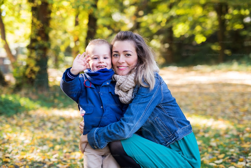 Beautiful young mother with small toddler son on a walk in autumn forest, resting.