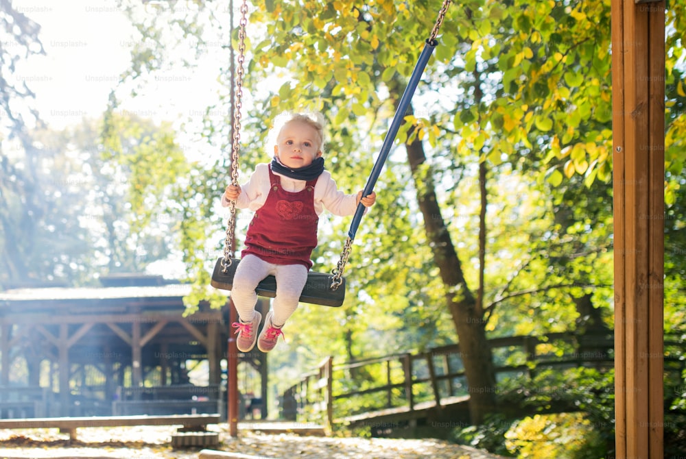 A front view of a small toddler girl on a swing on a playground.