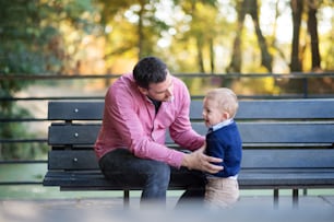 Un padre con figlio piccolo seduto sulla panchina nel parco in autunno.