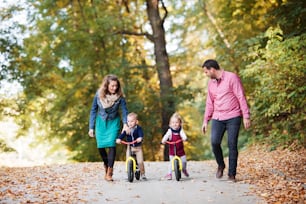A beautiful young family with small twins on a walk in autumn forest, riding balance bikes.