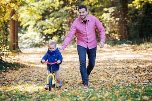 Front view of father and small son with a balance bike on a walk in autumn forest.