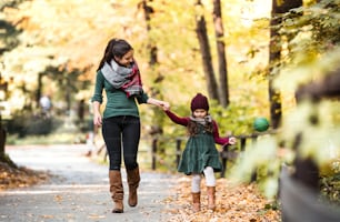 A portrait of young mother with a toddler daughter walking in forest in autumn nature, holding hands.