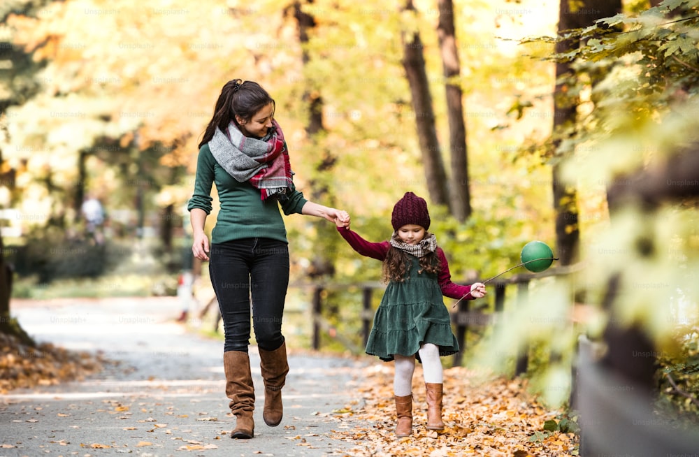 Ein Porträt einer jungen Mutter mit einer kleinen Tochter, die in der herbstlichen Natur Händchen haltend im Wald spazieren geht.