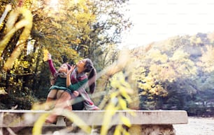 A mother with a toddler daughter sitting on wall in forest in autumn nature.