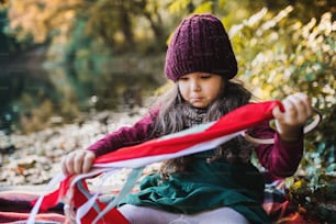 Portrait d’une petite fille en bas âge assise dans la forêt dans la nature automnale jouant avec un cerf-volant ruban.