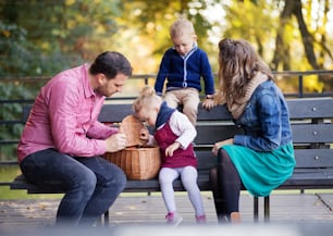 Eine schöne junge Familie mit kleinen Zwillingen auf einem Spaziergang im Herbstpark, auf einer Bank sitzend.